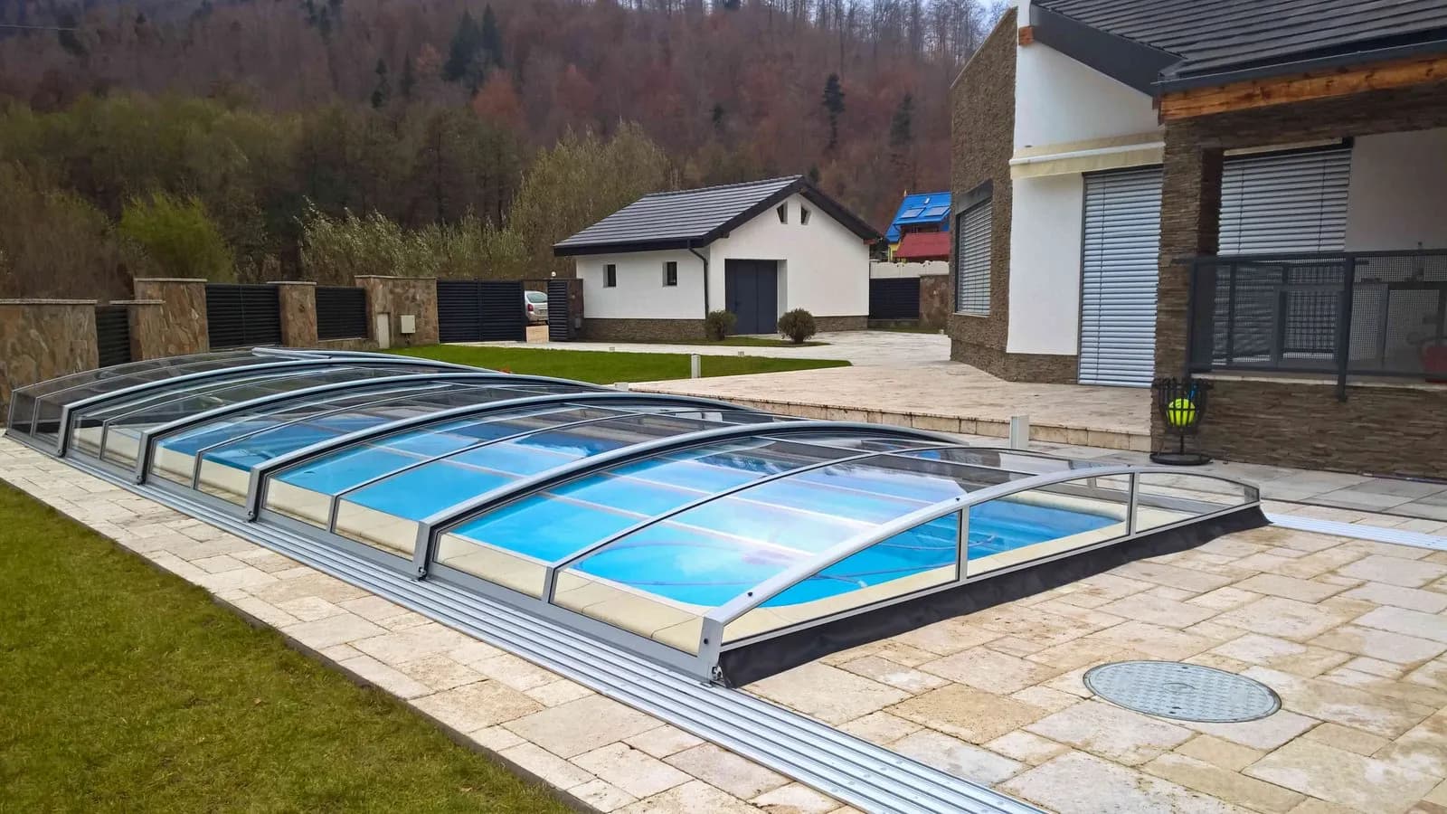 Alacsony, ezüst keretes íves alumínium medencefedés modern villa kertjében